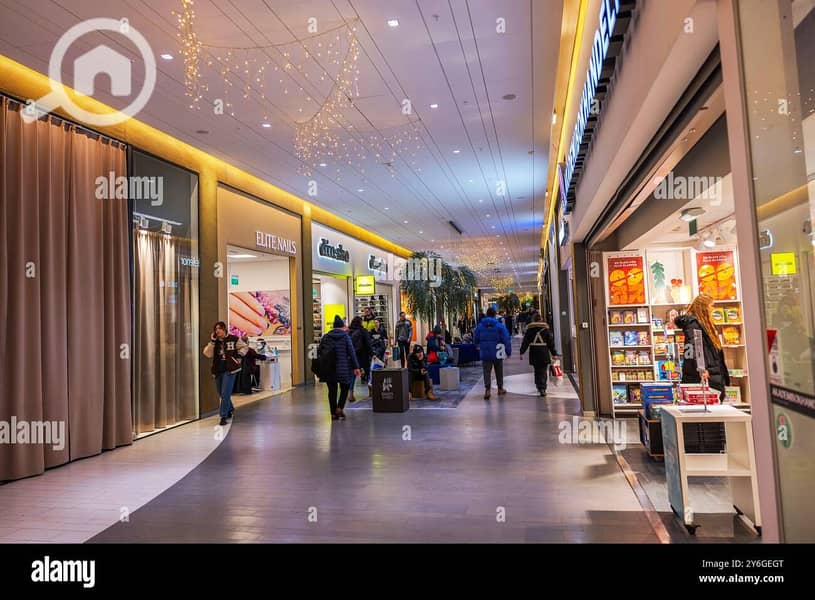 9 shoppers-walking-through-a-brightly-lit-shopping-mall-with-boutiques-and-christmas-decorations-hanging-above-2Y6GEGT. jpg